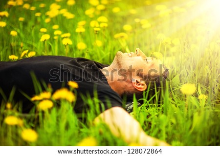 stock-photo-happy-smiling-man-lying-on-grass-with-yellow-dandelion-at-sunny-day-128072864.jpg